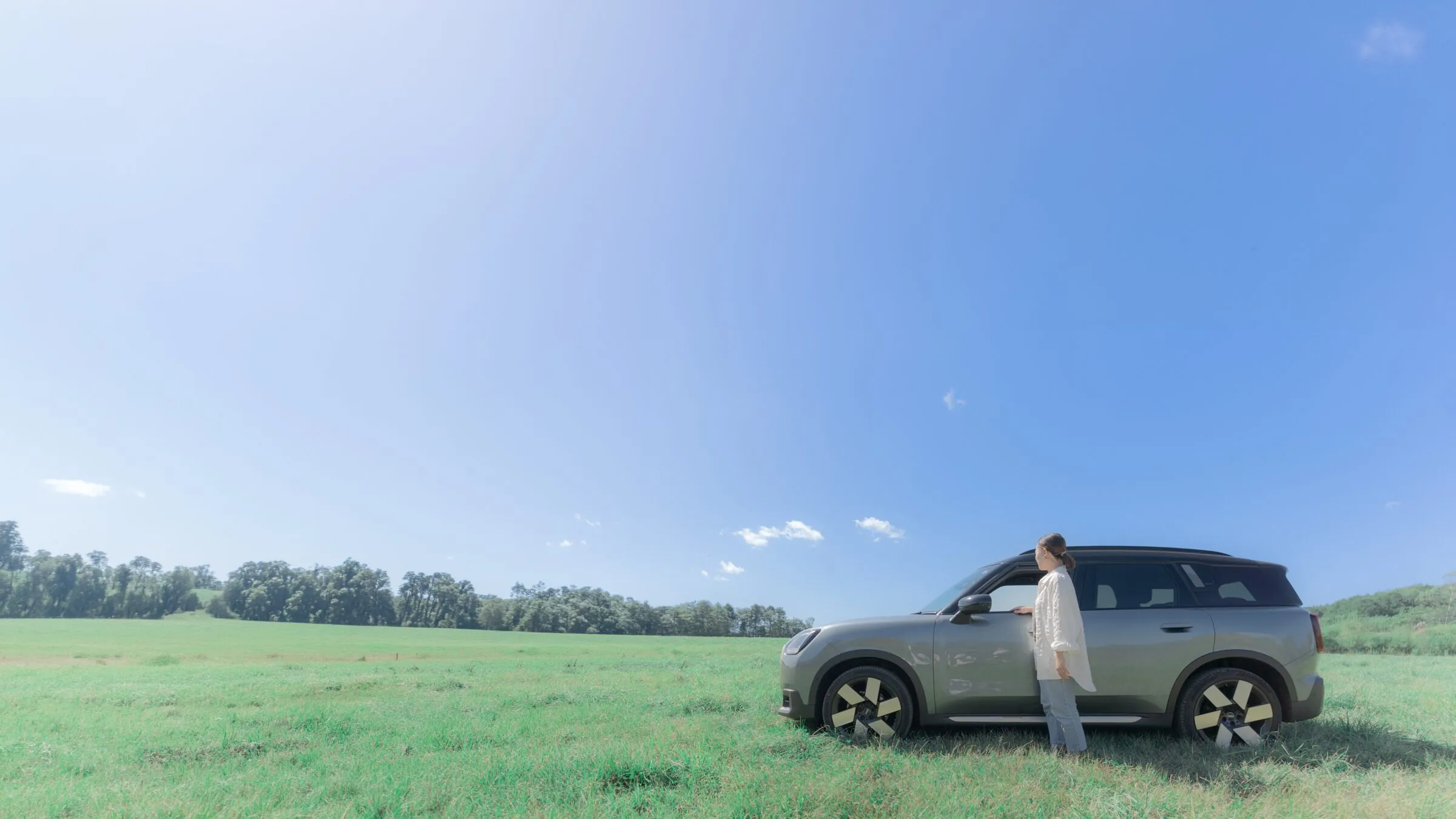 広い青空と牧草地、車の横に立つ女性